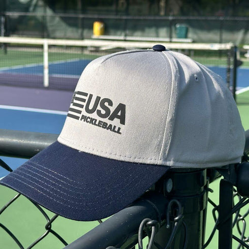 Gray and navy cap with 'USA Pickleball' logo on a pickleball court.